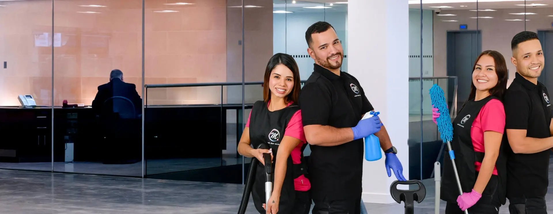 Vier Mitarbeitende von Multi Clean Service mit Staubsauger, Moppwagen und Staubwedel in der verglasten Lobby eines Bürogebäudes