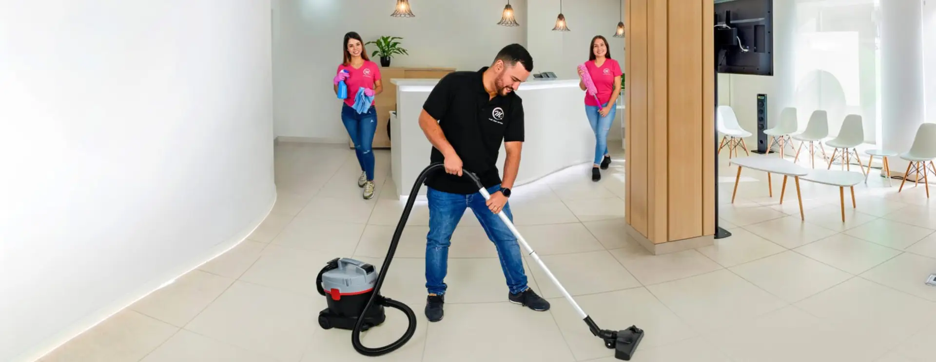 Drei Mitarbeitende von Multi Clean Service in einem Empfangs- und Wartebereich, einer saugt den Boden