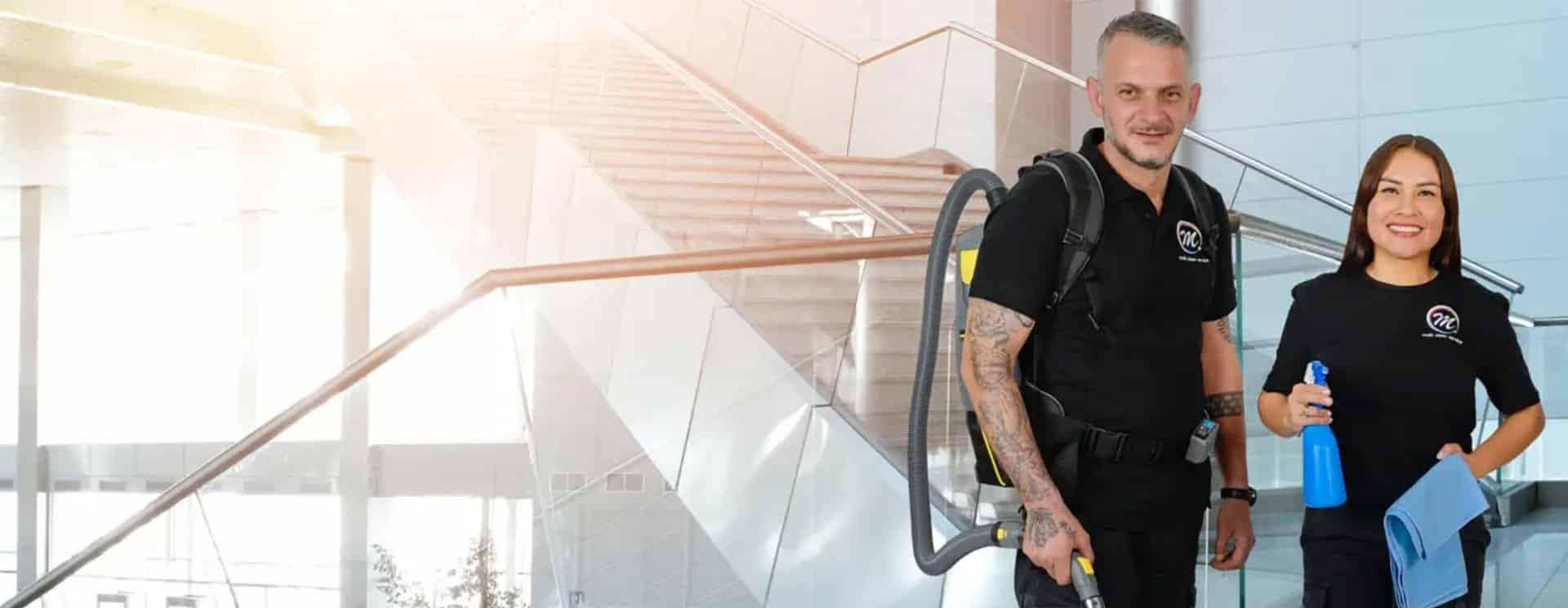 Zwei Mitarbeitende von Multi Clean Service in einem hellen Treppenhaus mit Glasgeländer, einer mit Rückensauger