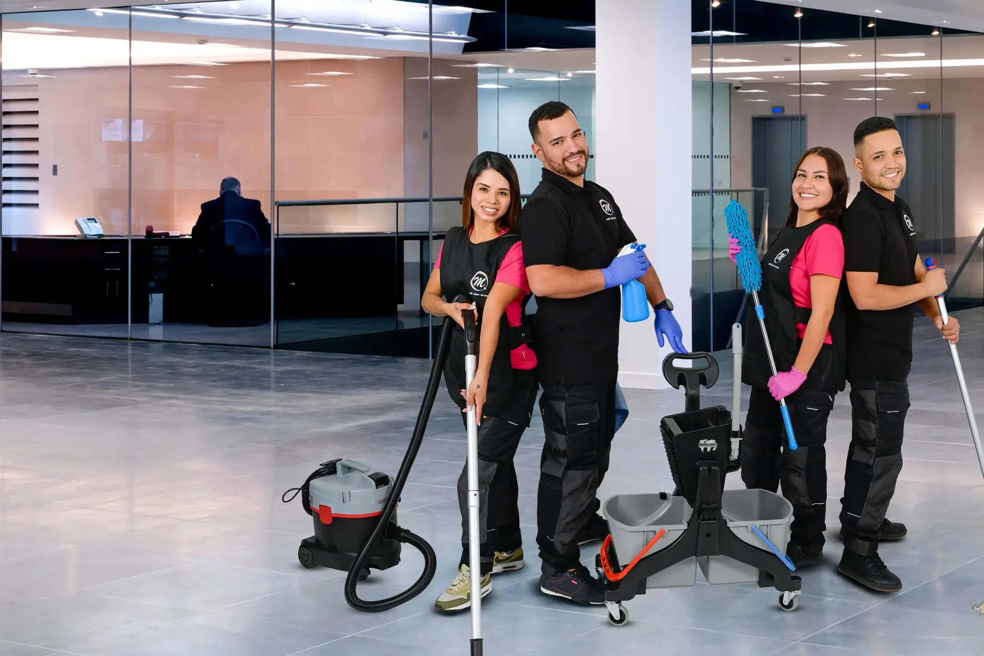 Unterhaltsreinigung Zürcher Oberland — Vier Mitarbeitende von Multi Clean Service mit Sauger, Moppwagen und Staubwedel in der Lobby eines Bürogebäudes